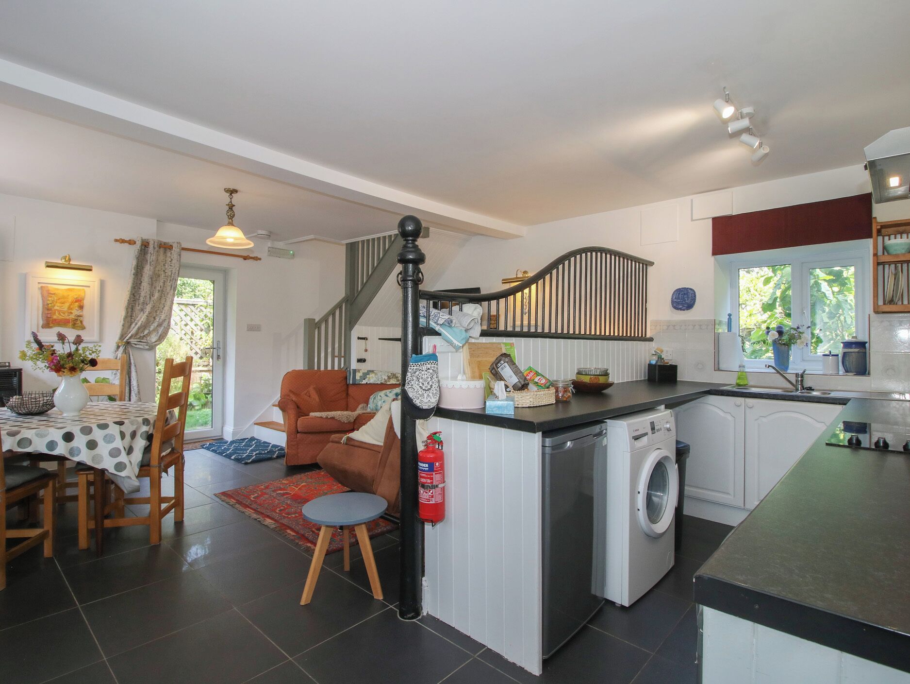 A kitchen with a washing machine, a dining area with a table and chairs, and a staircase.