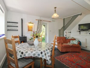 A dining area with a table, chairs, a vase with flowers, a fireplace, a sofa, a TV, and a staircase. - Chess Cottage (Hereford)