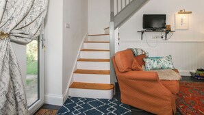 A staircase with wooden steps leading to a landing, a television mounted on the wall, and a cozy seating area with a patterned rug and cushions. - Chess Cottage (Hereford)
