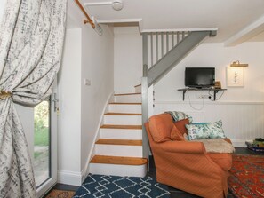 Eine Treppe mit Holzstufen führt zu einer Empore, an der Wand ist ein Fernseher angebracht, und es gibt eine gemütliche Sitzecke mit einem gemusterten Teppich und Kissen.