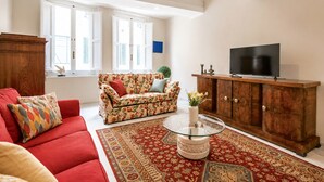 A living room with a red sofa, a floral sofa, a glass coffee table, a wooden cabinet, and a television. - Designer Home in Center Town (Lucca)