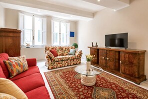 Ein Wohnzimmer mit einem roten Sofa, einem blumigen Sofa, einem Glastisch, einem Holzschrank und einem Fernseher.