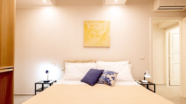 A bedroom with a bed, nightstands, a lamp, a wall-mounted artwork, and a door. - Designer Home in Center Town (Lucca)