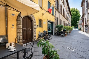 Eine enge Straße mit einem Café, Außenbestuhlung, einem steinernen Bogen und einer Reihe geparkter Fahrräder.