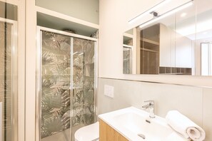 A bathroom with a glass shower enclosure, a white sink, and a mirror above the sink. - Designer Home in Center Town (Lucca)