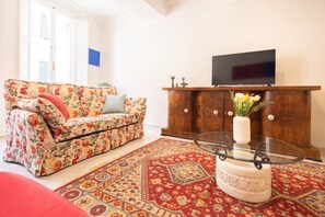 A living room with a floral sofa, a television on a wooden cabinet, and a patterned rug. - Designer Home in Center Town (Lucca)