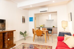 A modern living room with a TV, dining table, chairs, a red sofa, and a kitchen in the background. - Designer Home in Center Town (Lucca)
