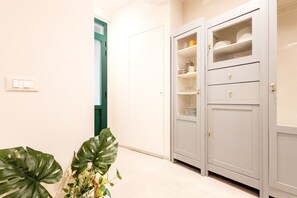 Ein Flur mit einer weißen Tür, einer Pflanze und einem grauen Schrank mit Regalen.