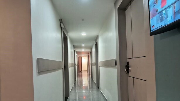 A long, narrow hotel corridor with a flat floor, recessed lighting, and a television mounted on the wall. - Hotel Satyam (Vadodara)