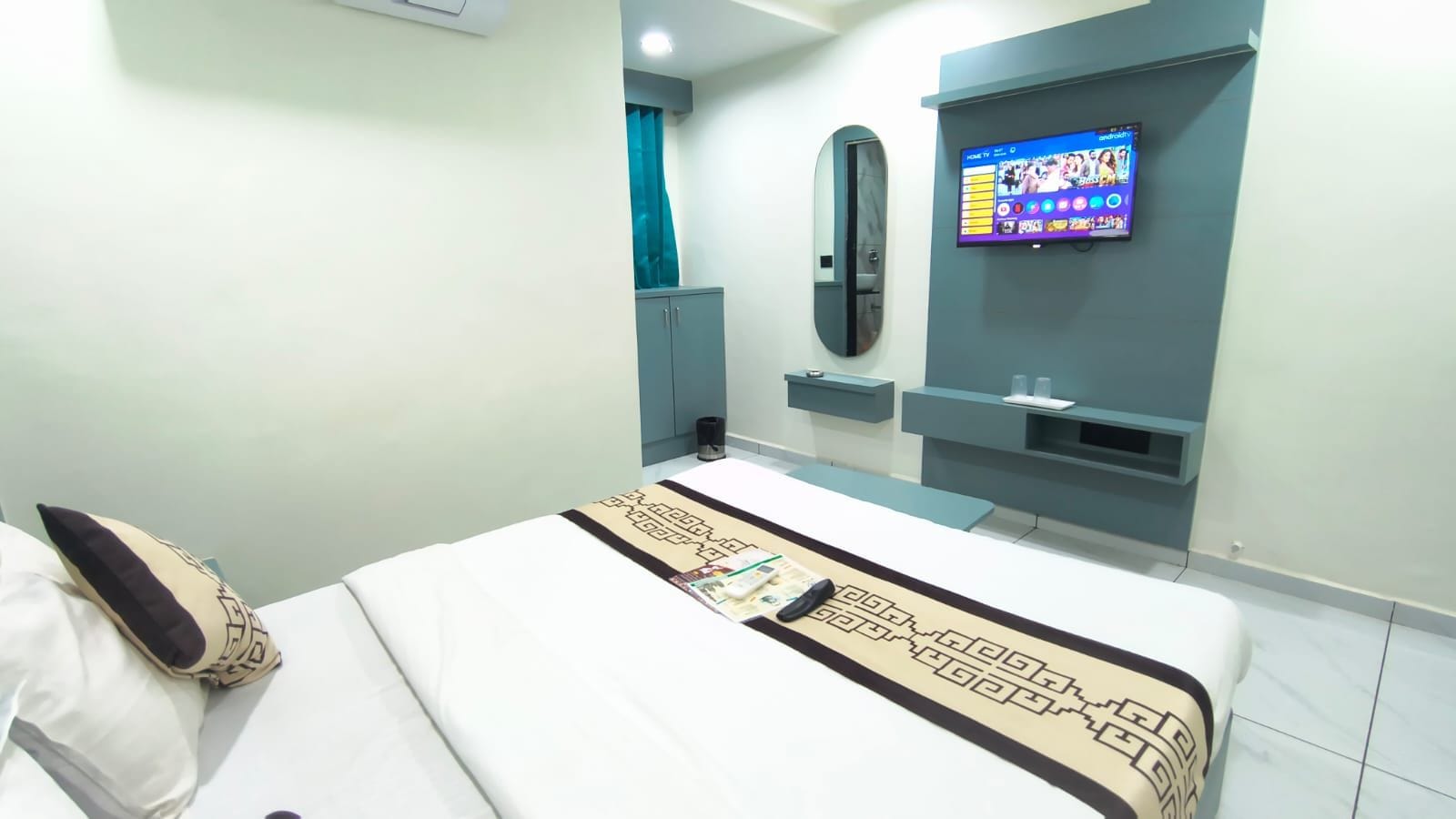 Habitación de hotel con cama, televisor montado en la pared, espejo y mesita de noche.
