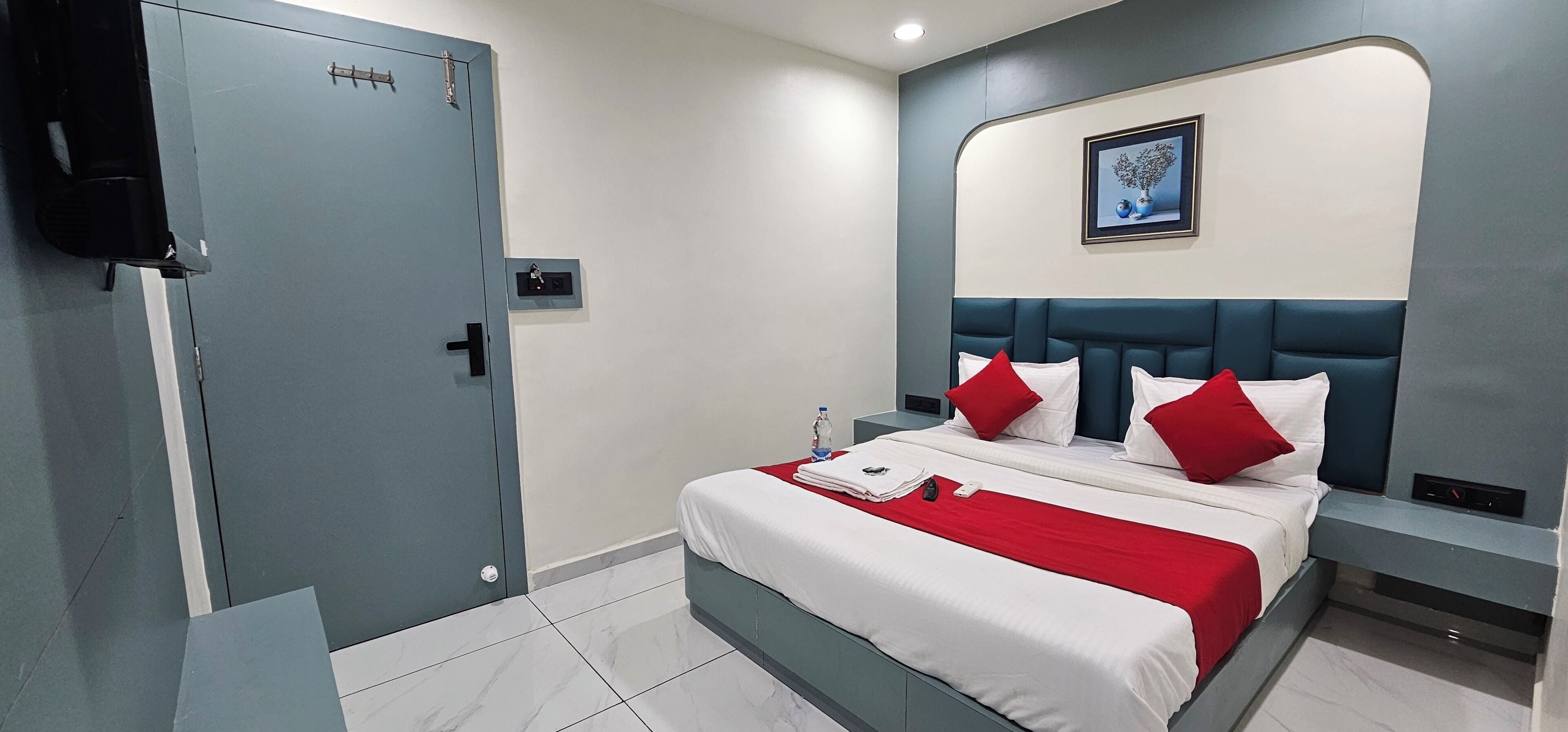 A hotel room with a bed, a nightstand, a wall-mounted picture, and a door with a handle.