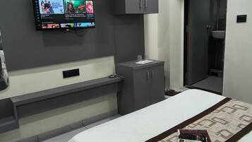 Quarto de hotel moderno com cama, televisão presa à parede, mesa de cabeceira e guarda-roupa.