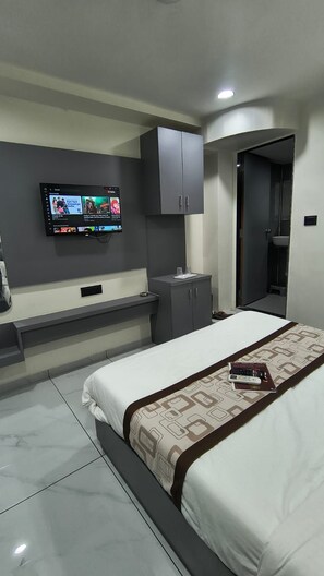 A modern hotel room with a bed, a TV mounted on the wall, a bedside table, and a wardrobe.