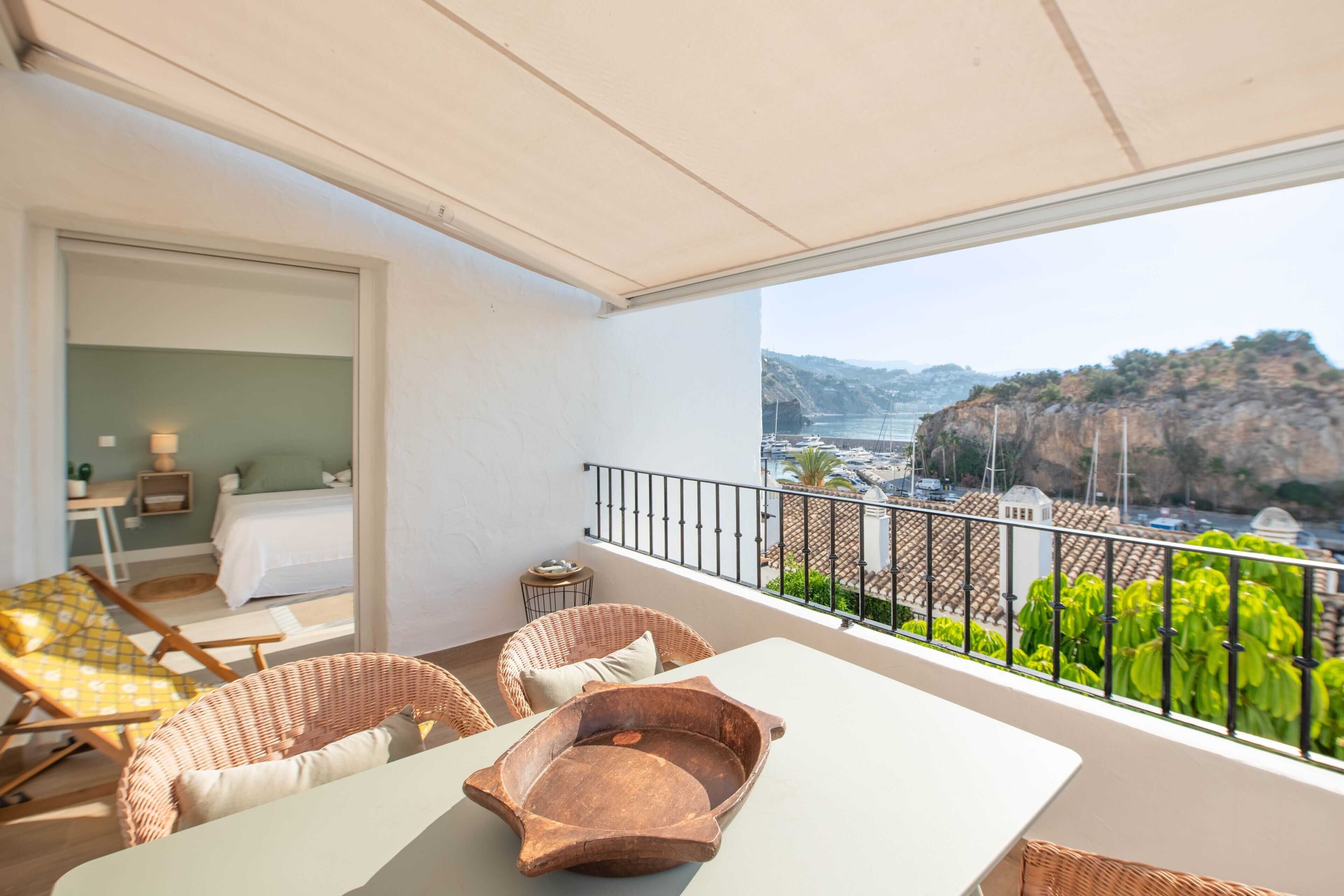 A balcony with wicker furniture, a table, and a view of a coastal landscape.