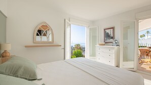 Quarto com cama, penteadeira, espelho e varanda com mobiliário para área externa.