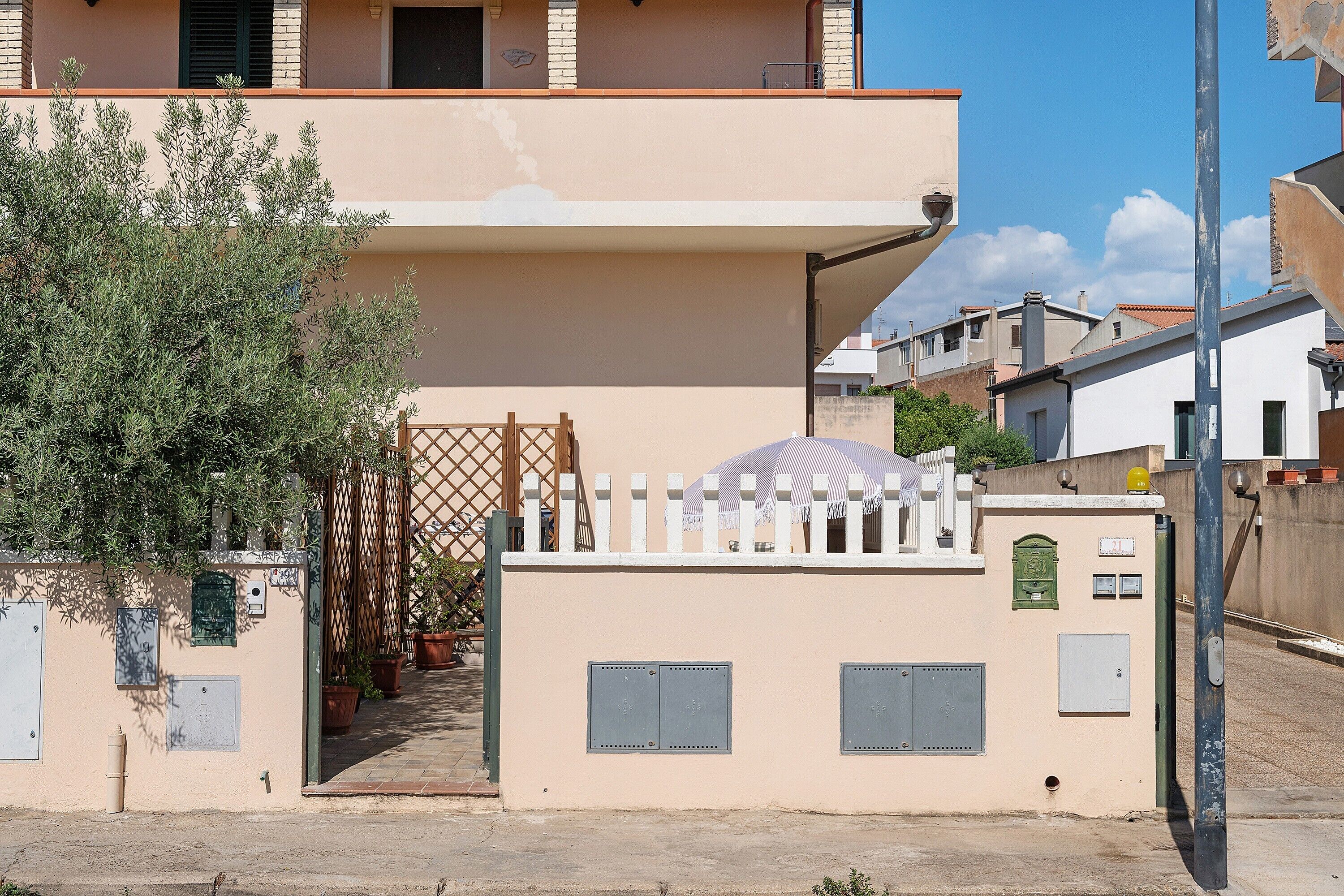 A residential building with a gated entrance, a small covered outdoor seating area, and a visible utility meter.