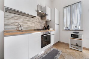 Una cocina moderna con armarios blancos, encimera de madera, horno empotrado y un microondas pequeño.