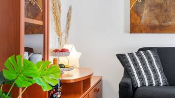 Une pièce avec un buffet en bois, une lampe, un panier de fruits et un canapé agrémenté d’un coussin à motifs.
