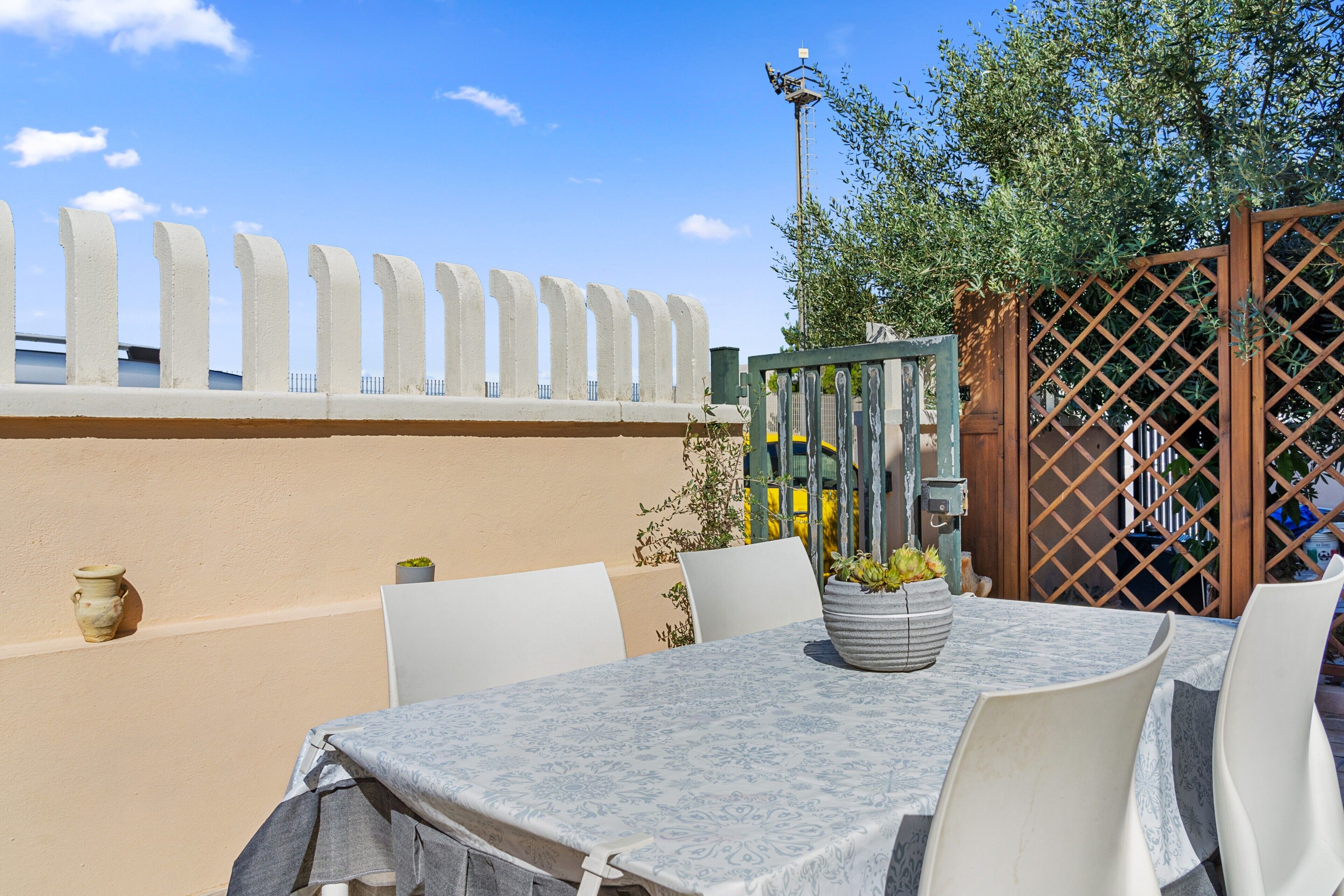 An outdoor dining area with a table and chairs, a potted plant, and a fence.