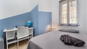 Ein Schlafzimmer mit einem Bett, einem Schreibtisch mit Globus, einem Stuhl, einer Lampe und einem Fenster mit Vorhang.