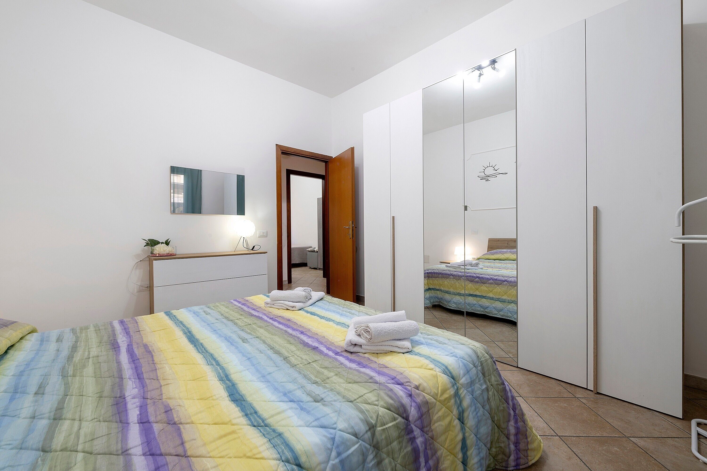 A bedroom with a bed, a wardrobe, a mirror, and a bathroom visible through an open door.