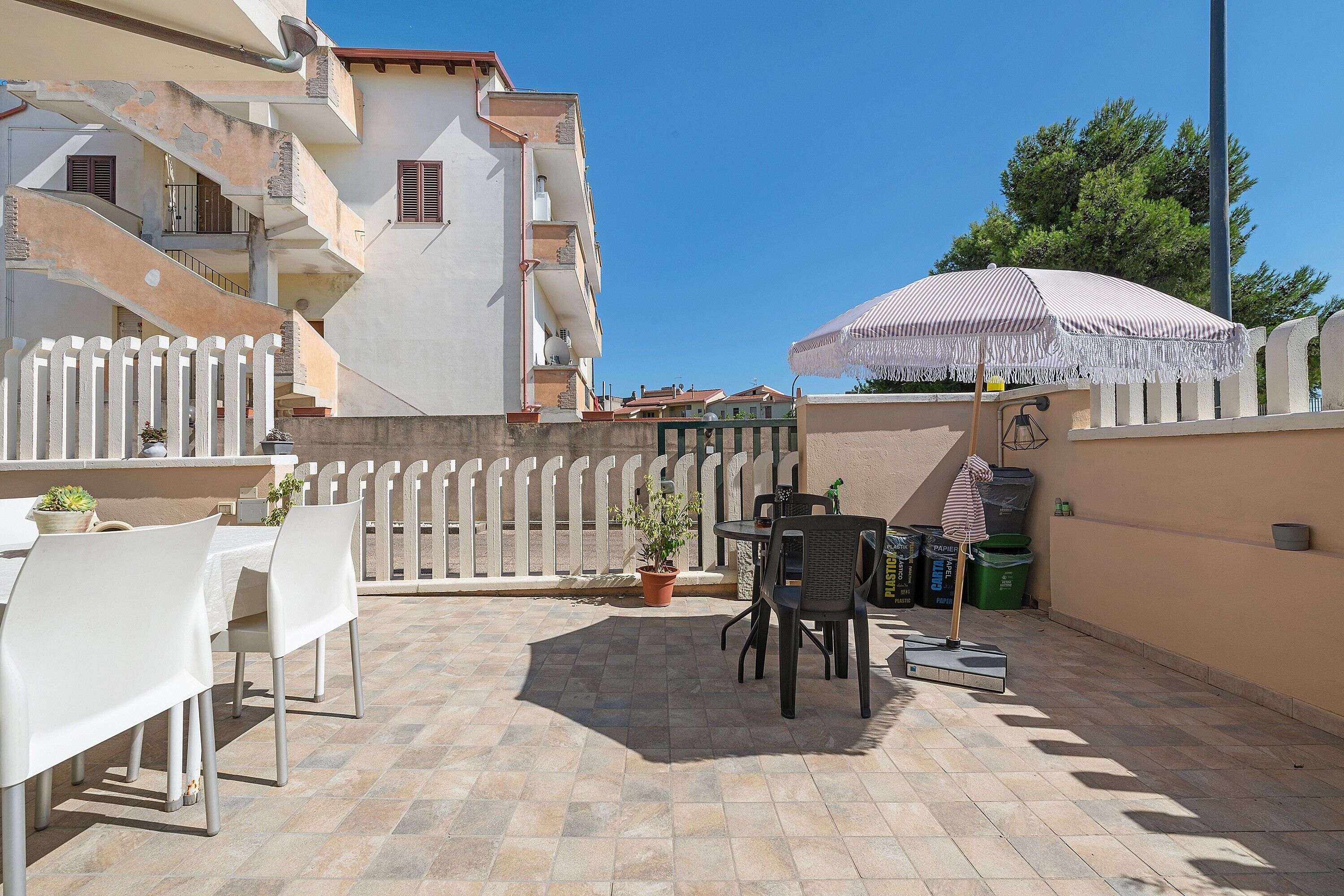 Une terrasse extérieure avec une table et des chaises, un pot de fleurs et un parasol à rayures.