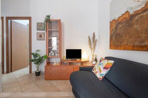 Un saló amb un sofà fosc, un armari de fusta amb portes de vidre, una televisió i una planta en test.