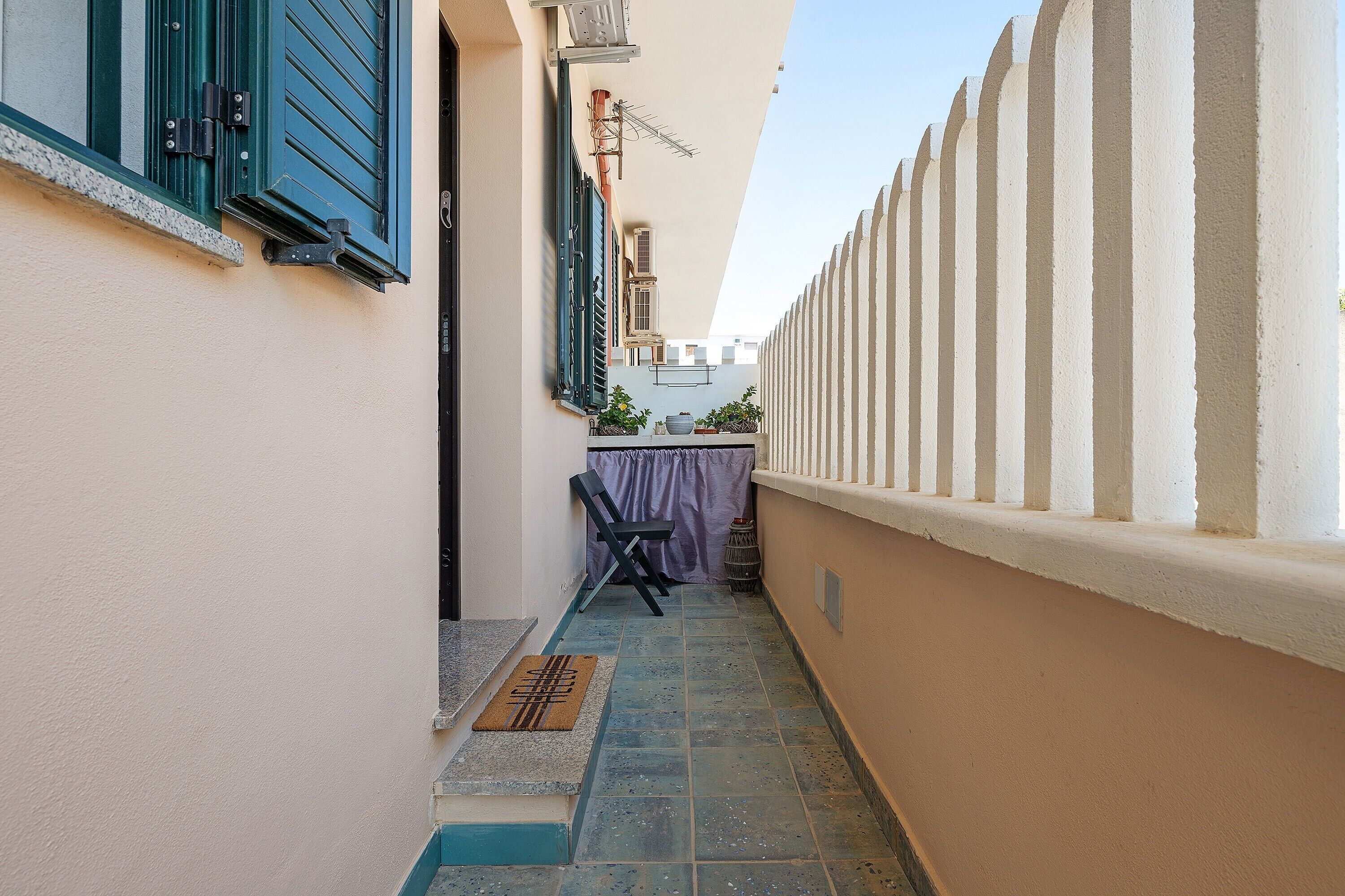 A narrow outdoor corridor with a tiled floor, a chair, and a table with a purple tablecloth.