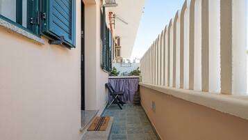 A narrow outdoor corridor with a tiled floor, a chair, and a table with a purple tablecloth.