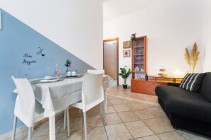 A dining area with a table set for two, a sofa, and a cabinet with glassware. - Casa Bea – Comfort and Relaxation in the Heart of Dolianova (Dolianova)