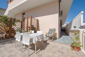Un patio al aire libre con una mesa, sillas y macetas con plantas.