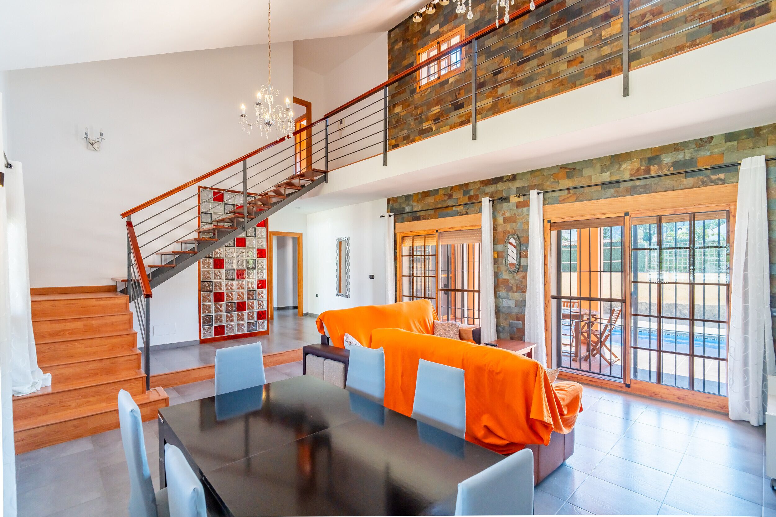 En rummelig opholdsstue med spisebord, orange sofa og trappe til en etage over.