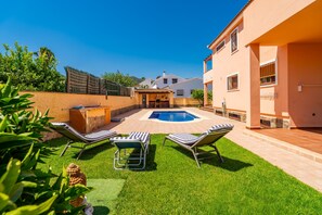 Un jardin avec une piscine, deux chaises longues et un petit espace barbecue.
