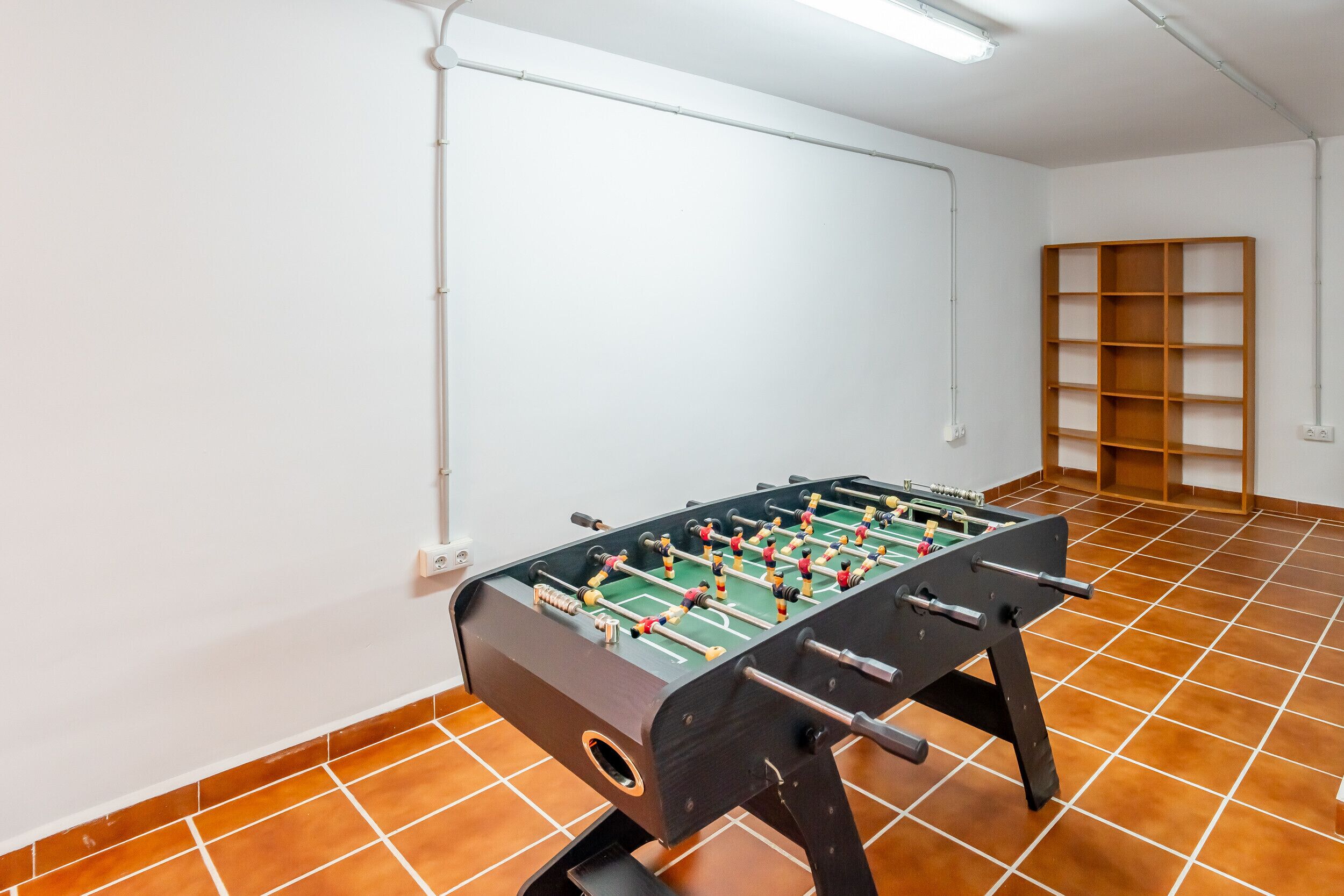 A room with a foosball table, a shelf, and a tiled floor.