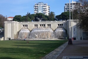 Ein großer öffentlicher Brunnen mit mehreren Stufen, umgeben von einer gepflegten Rasenfläche und einer Steinmauer.