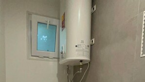 A small bathroom with a toilet, a sink, and a water heater mounted above the toilet. - A haven in the heart of Lisbon—just 4 minutes from the Metro. Double and quadruple rooms. (Lisboa)