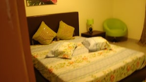 Un llit amb roba de llit floral, una tauleta de nit amb una làmpada i una cadira verda en una habitació amb un capçal marró.