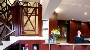 Una reception con un bancone in legno e un vaso di fiori. Si vede una scala con ringhiere in legno e un certificato incorniciato appeso al muro.
