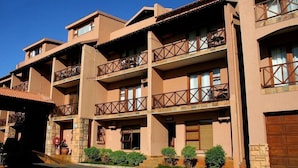 Un hotel a più piani con balconi, facciata in pietra e un’area di parcheggio.