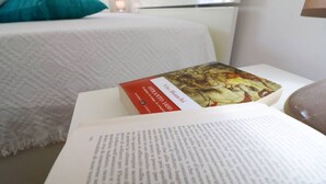 Una camera d'albergo con un letto, un comodino con un libro e una lampada.