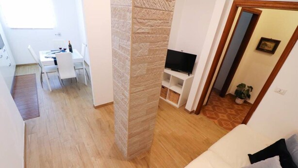 Un soggiorno con divano bianco, televisore su supporto, zona pranzo con tavolo e sedie, e una parete decorata in pietra.