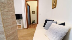 Un soggiorno con un divano, una TV su un mobile, una porta che conduce in un'altra stanza e un quadro appeso al muro.
