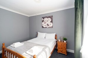 Une chambre à coucher comprenant un lit, une table de chevet, une commode et une œuvre d’art accrochée au mur.