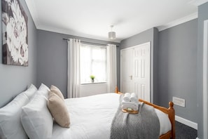 A bedroom with a bed, white curtains, a window with a view, a door, and a ceiling light.