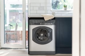 A compact, modern laundry room with a front-loading washing machine, a small window with a plant, and a door leading to an outdoor area.