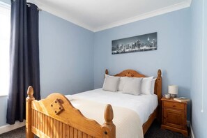 A bedroom with a wooden bed, a nightstand, a lamp, and a cityscape painting on the wall. - Comfortable 3 Bed House nr Chesterfield w Garden (Doe Lea)