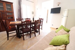 Ein Essbereich mit einem Holztisch und Stühlen, einem an der Wand montierten Fernseher und einem Sofa mit grünen Kissen.