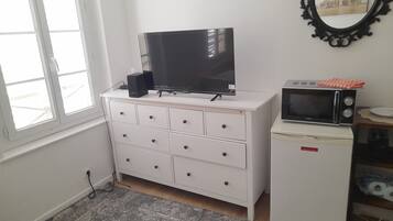 Een kamer met een witte ladekast, een flatscreen televisie, een magnetron en een kleine koelkast.
