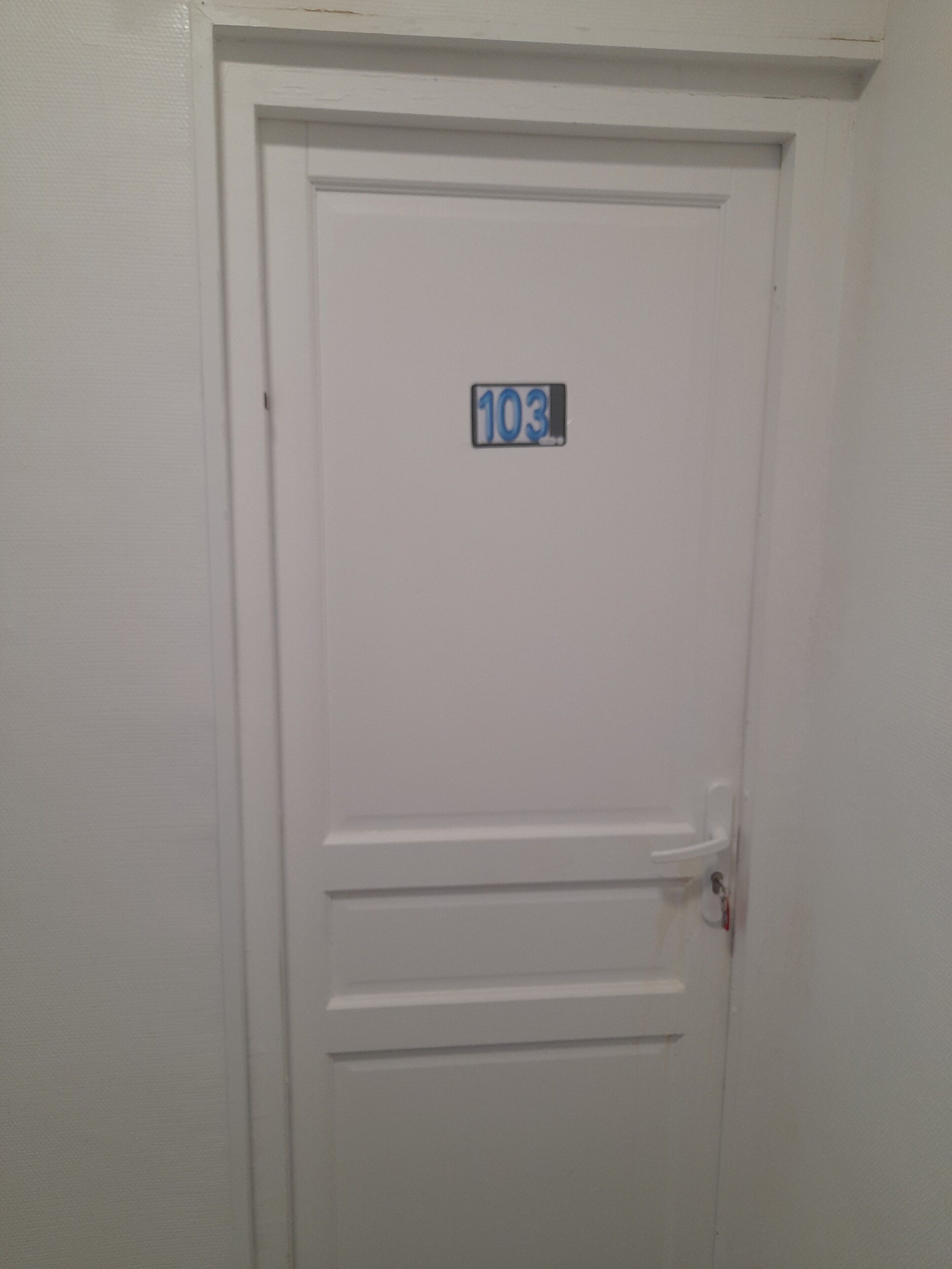 Een witte deur met een nummerbord waarop kamer 103 staat.
