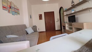 Ein Wohnzimmer mit einer Couch, einem Fernseher auf einem Schrank, einer Tür und einer Wand mit abstrakter Kunst.